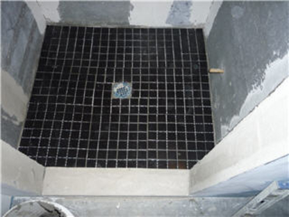 Shower floor mid-renovation with small black mosaic tile around a drain